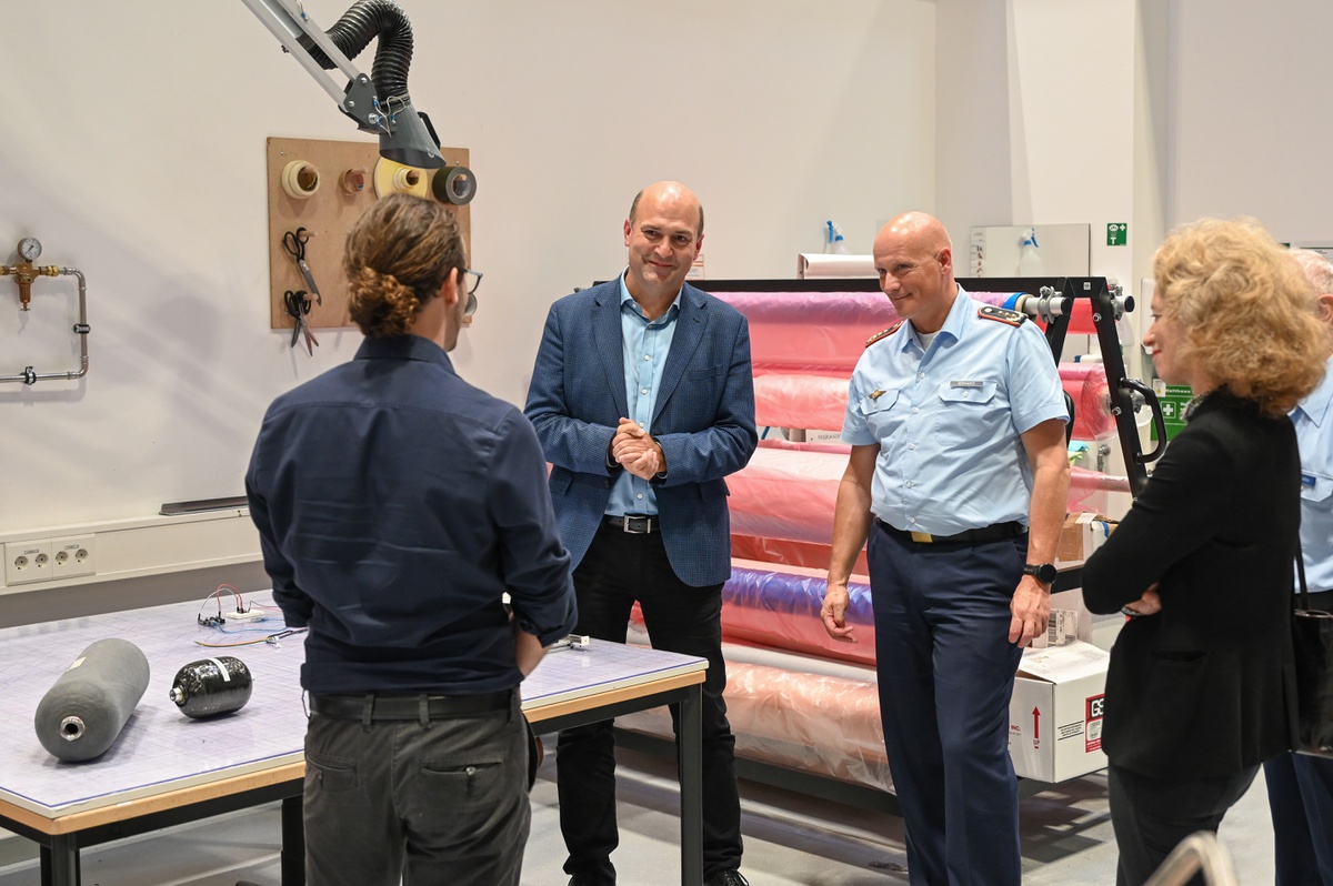 Im Hintergrund von links nach rechts stehen Prof. Hupfer, Generalleutnant Gerhartz und Präsidentin Prof. Kern die Herstellungsmöglichkeiten der Werkstätten von einem wissenschaftlichen Mitarbeiter erklären.