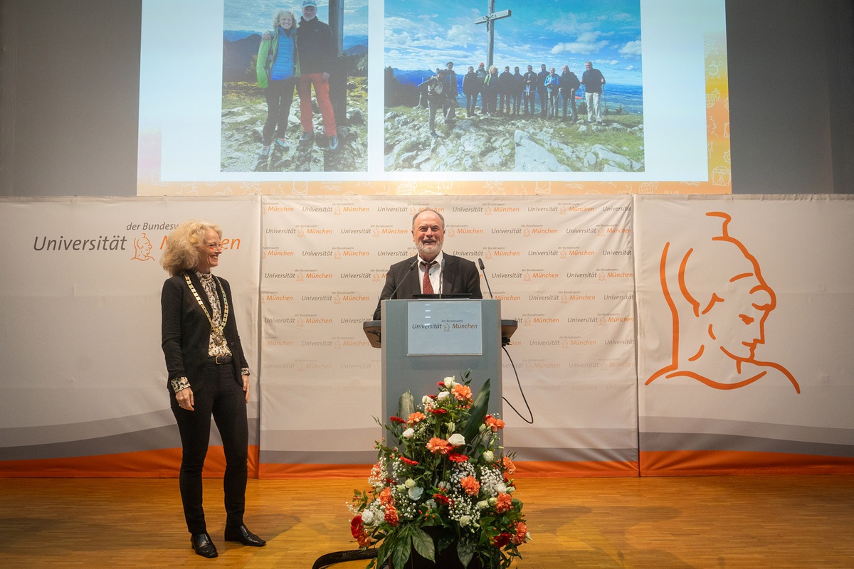 Prof. Borghoff am Rednerpult, neben ihm Präsidentin Kern. Im Hintergrund über den beiden wird eine Präsentation auf die Leinwand geworden: Links ein Bild von Prof. Kern und Prof. Borghoff in Outdoorkleidung auf einem Berggipfel, rechts ein Foto von einer Gruppe von Menschen auf einem Berggipfel