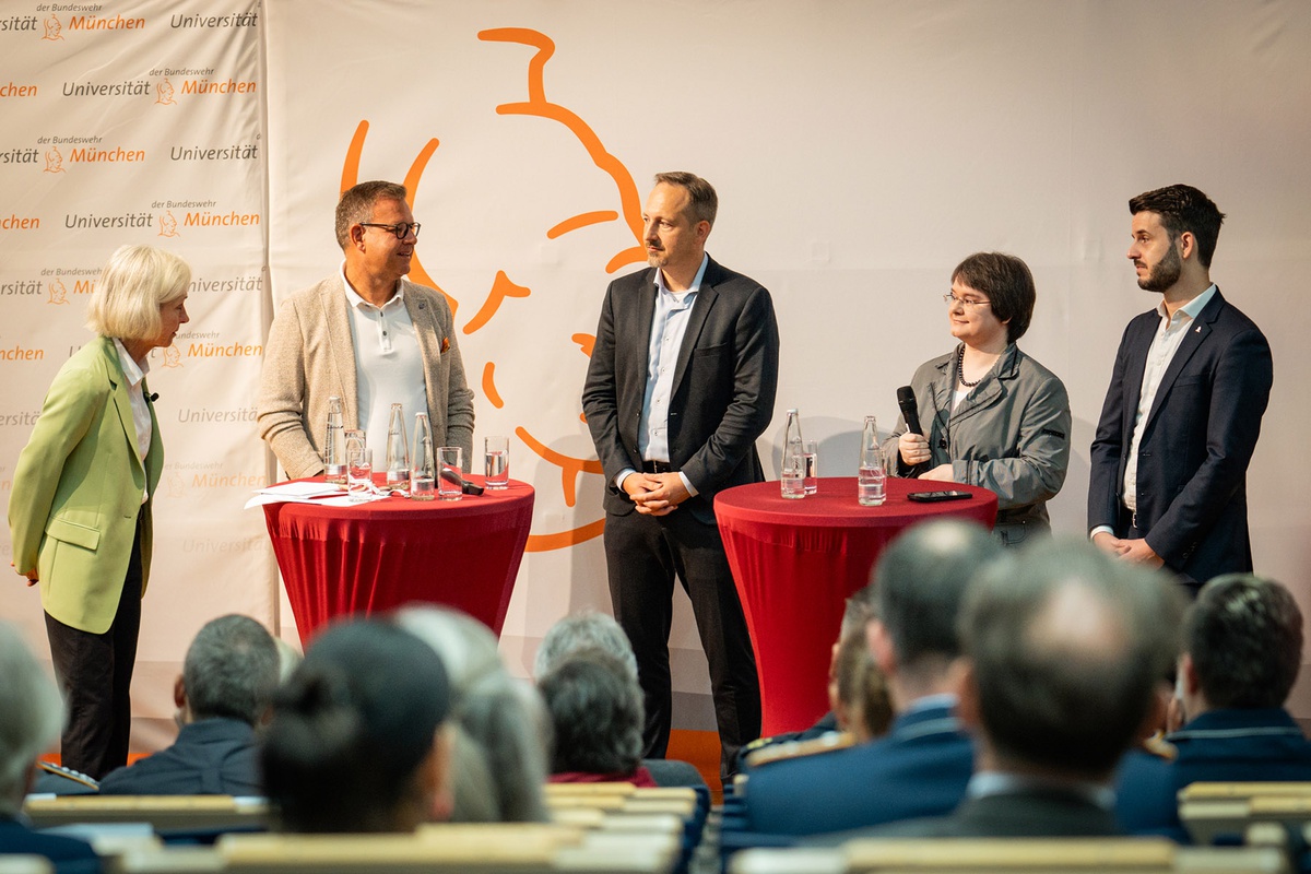 Prof. Münch, Prof. Trapp, Prof. Geierhos und Prof. Popp vorne auf dem Podium, im Bildvordergrund sind die Zuhörerenden von hinten zu sehen