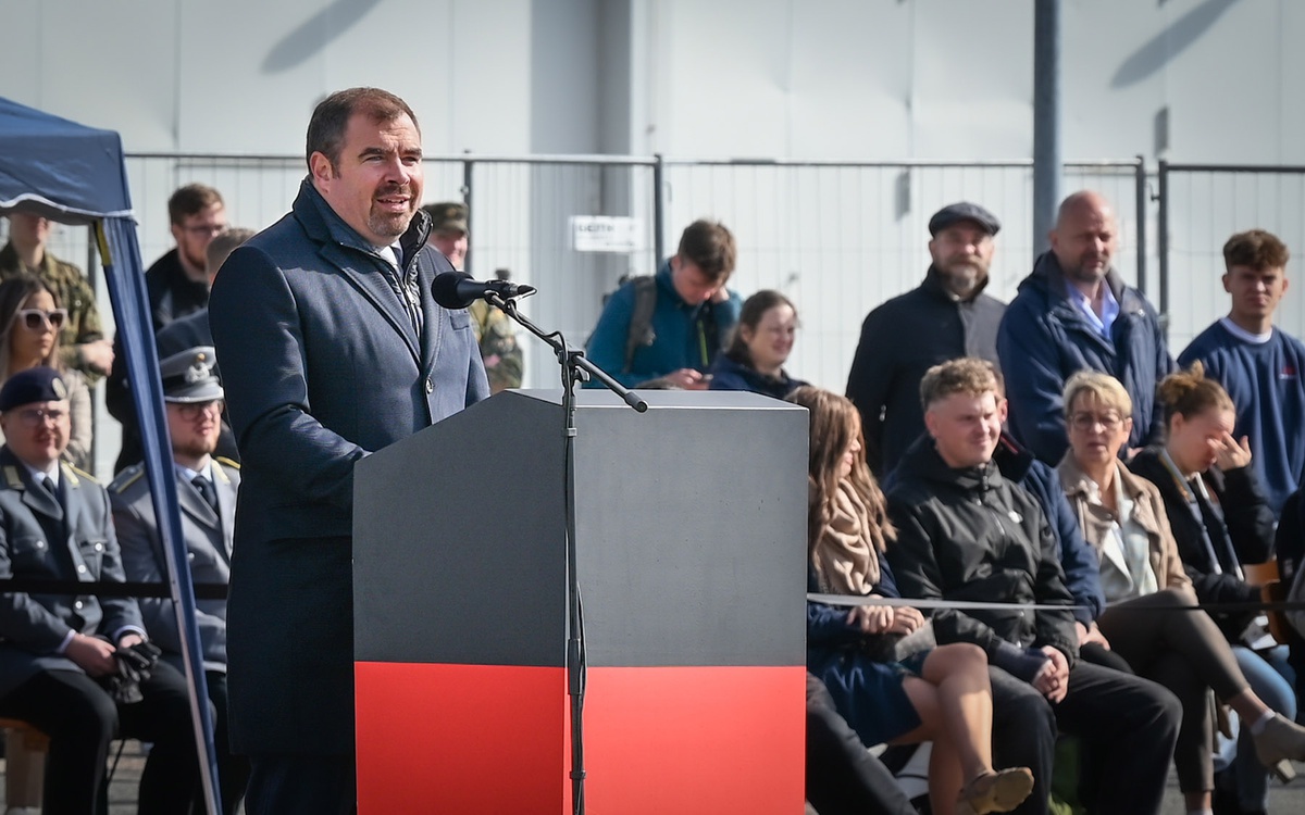 Florian Hahn steht an einem Rednerpult und spricht zu den Beförderten (nicht im Bild zu sehen). Hinter ihm sitzen auf Tribünen Zuschauerinnen und Zuschauer